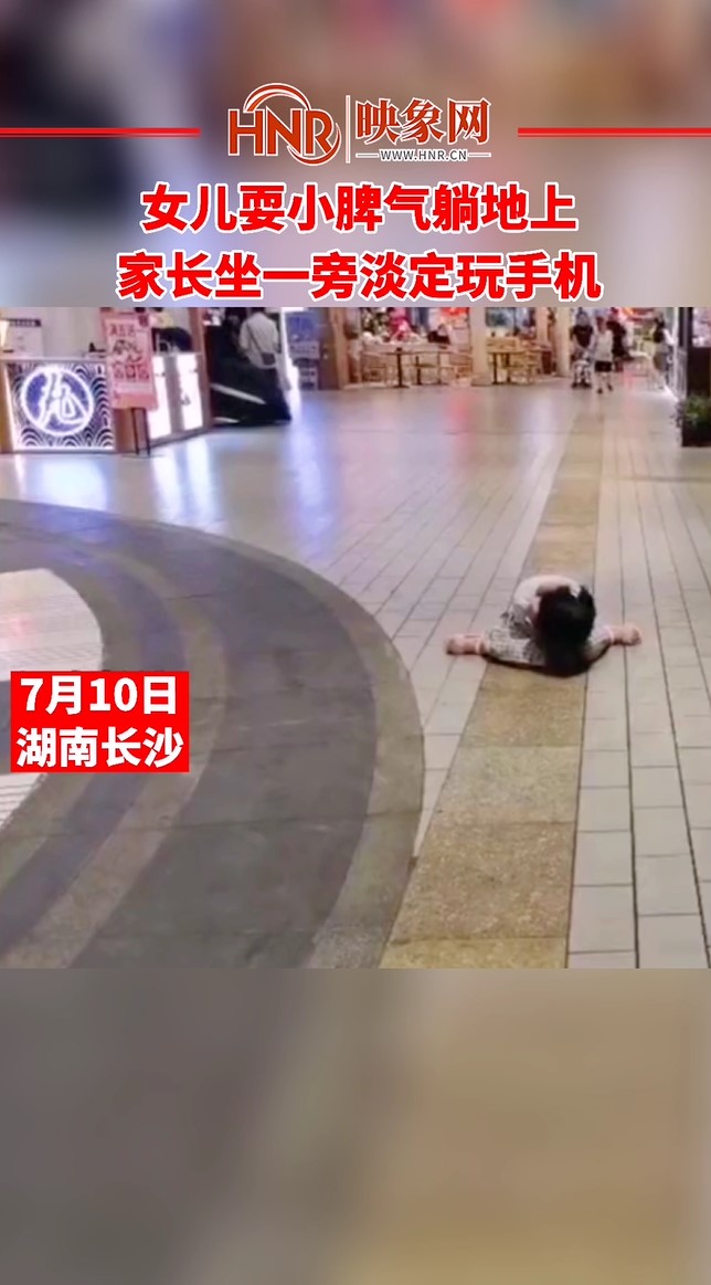 女儿耍小脾气躺地上 家长坐一旁淡定玩手机